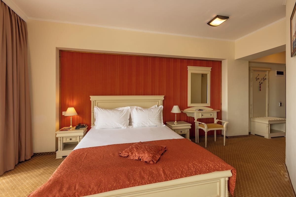 Una habitación de hotel con una cama grande, un escritorio, una silla, un espejo y un armario.