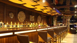 Eine Bar mit einer langen Theke, Korbstühlen und dekorativen Wandverkleidungen.