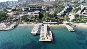 Luftaufnahme eines Küstenresorts mit einer Mole, Strand und einer Wohngegend an einem Hügel.