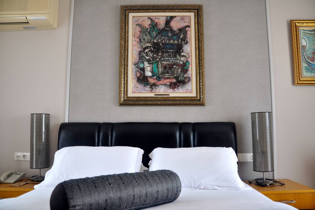 Une chambre d’hôtel avec un lit, deux lampes de chevet, un téléphone et une œuvre d’art encadrée au mur.