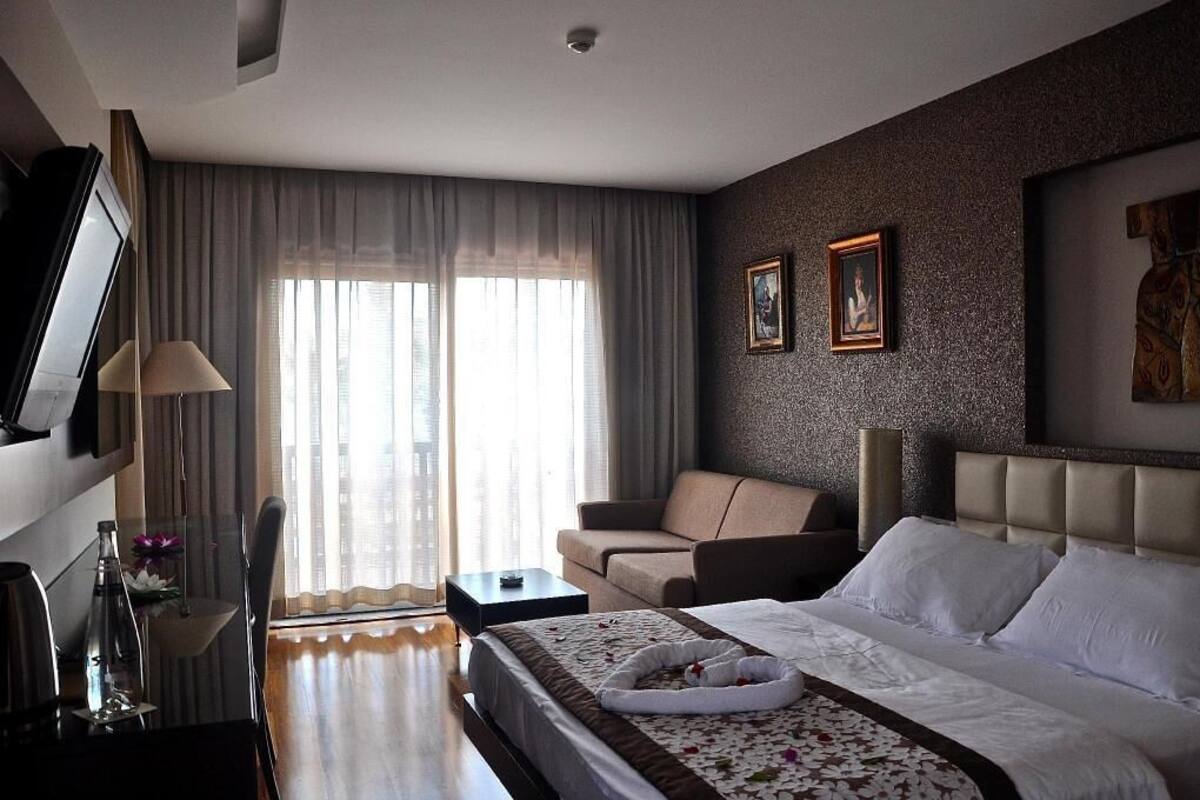 Une chambre d’hôtel avec un lit, un canapé, une télévision, un bureau et une fenêtre avec des rideaux.