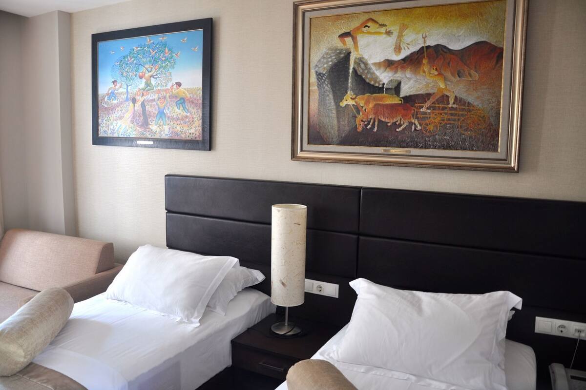 Une chambre d’hôtel avec deux lits, une table de chevet, une lampe et deux tableaux au mur.