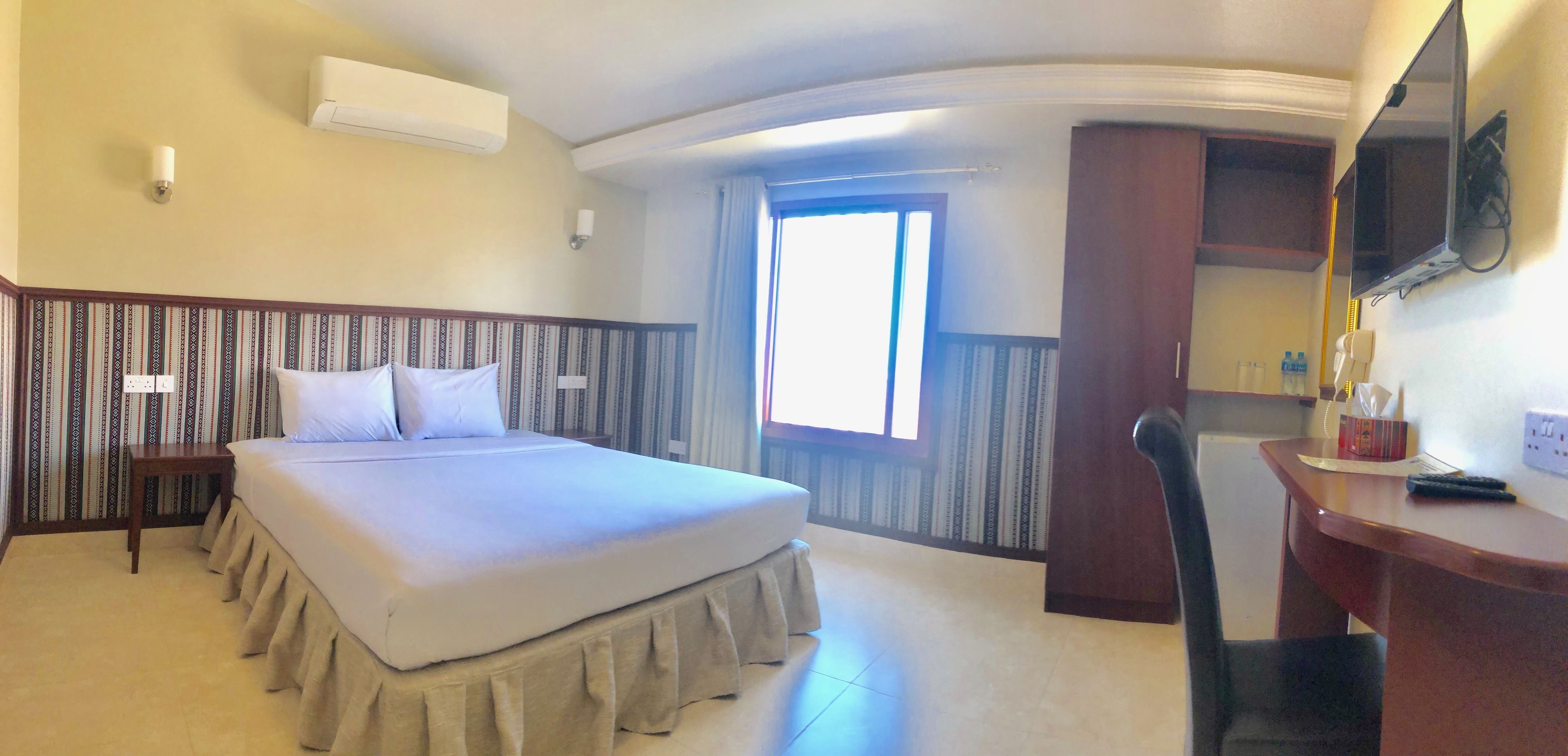 A hotel room with a bed, a desk, a chair, a TV, and a window.