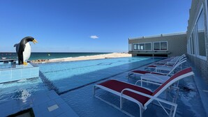 A pool area with lounge chairs, a penguin statue, and a view of the beach and ocean.