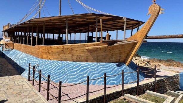 A wooden boat structure with a covered deck and a figurehead, surrounded by a decorative blue and white patterned area.