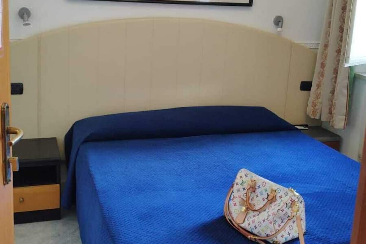 Una habitación con una cama, un cuadro colgado en la pared, una mesita de noche y una puerta.