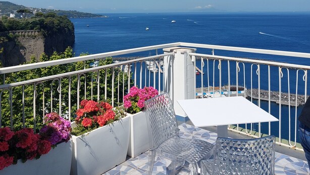 Een balkon met een tafel en stoelen, met uitzicht op de kust, boten en kliffen.