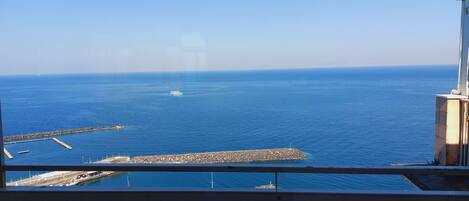 A marina with boats docked, a rocky breakwater, and a clear view of the sea.