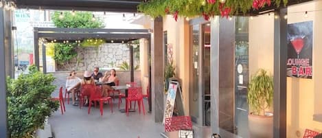 An outdoor patio area with red chairs and tables, a stone wall, and greenery.