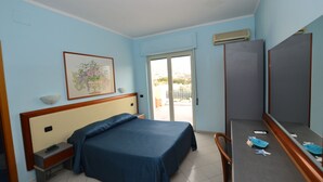 Een hotelkamer met een bed, een bureau, een stoel, een ingelijste foto aan de muur en een schuifpui naar het balkon.