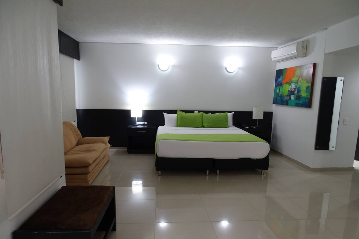 Een moderne hotelkamer met een groot bed, een slaapbank, een nachtkastje en een schilderij aan de muur.