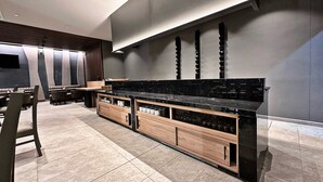 Zona bar moderna con un piano di lavoro nero, scaffali in legno e posti a sedere.