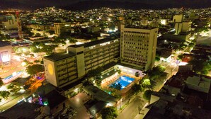 Un hotel di grattacielo con numerosi piani, una piscina sul tetto e un ambiente urbano ben illuminato.