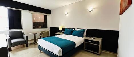 A hotel room with a bed, bedside tables, a desk, and a chair.