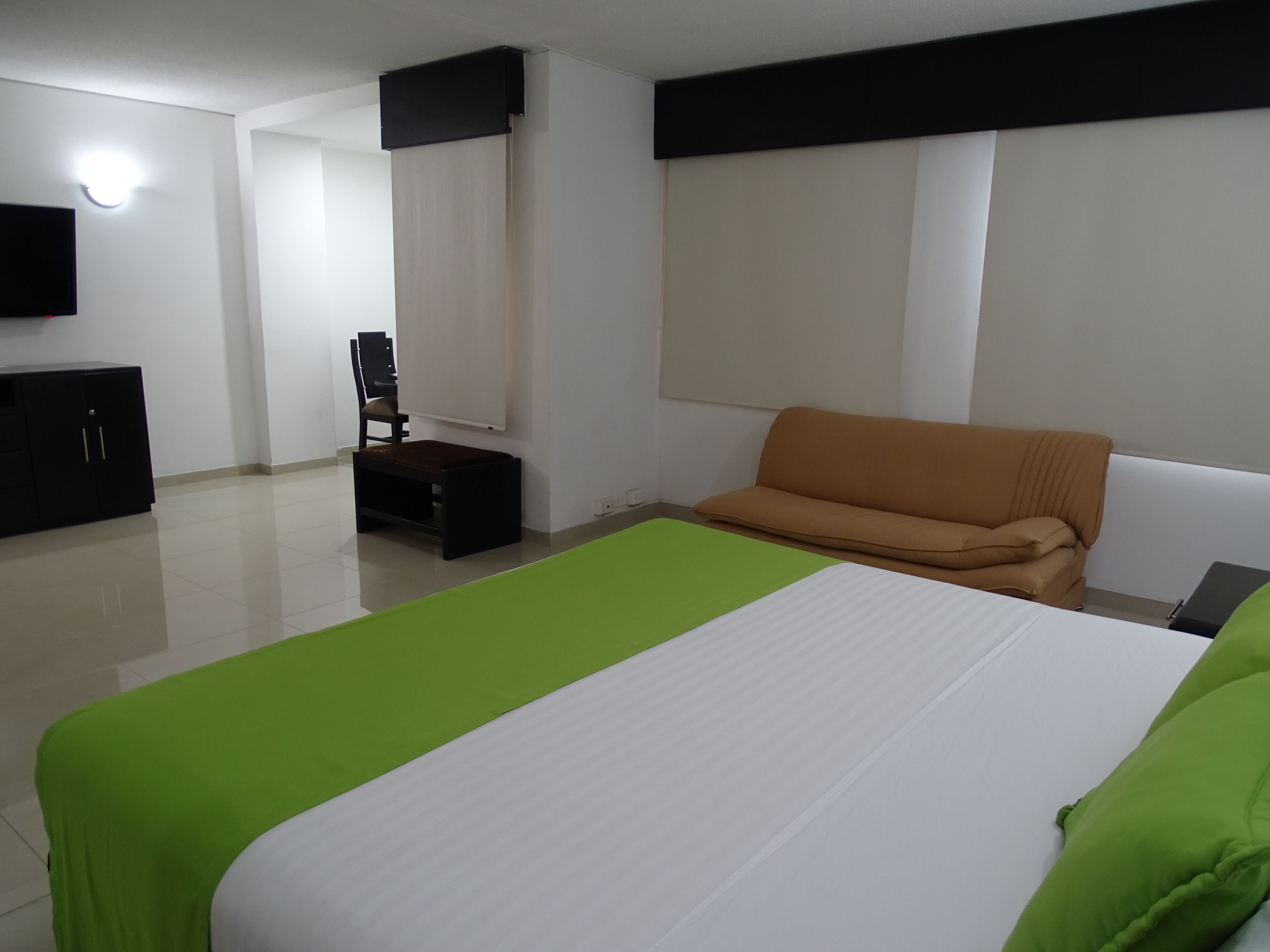 A hotel room with a bed, a sofa, a desk, a chair, and a TV.