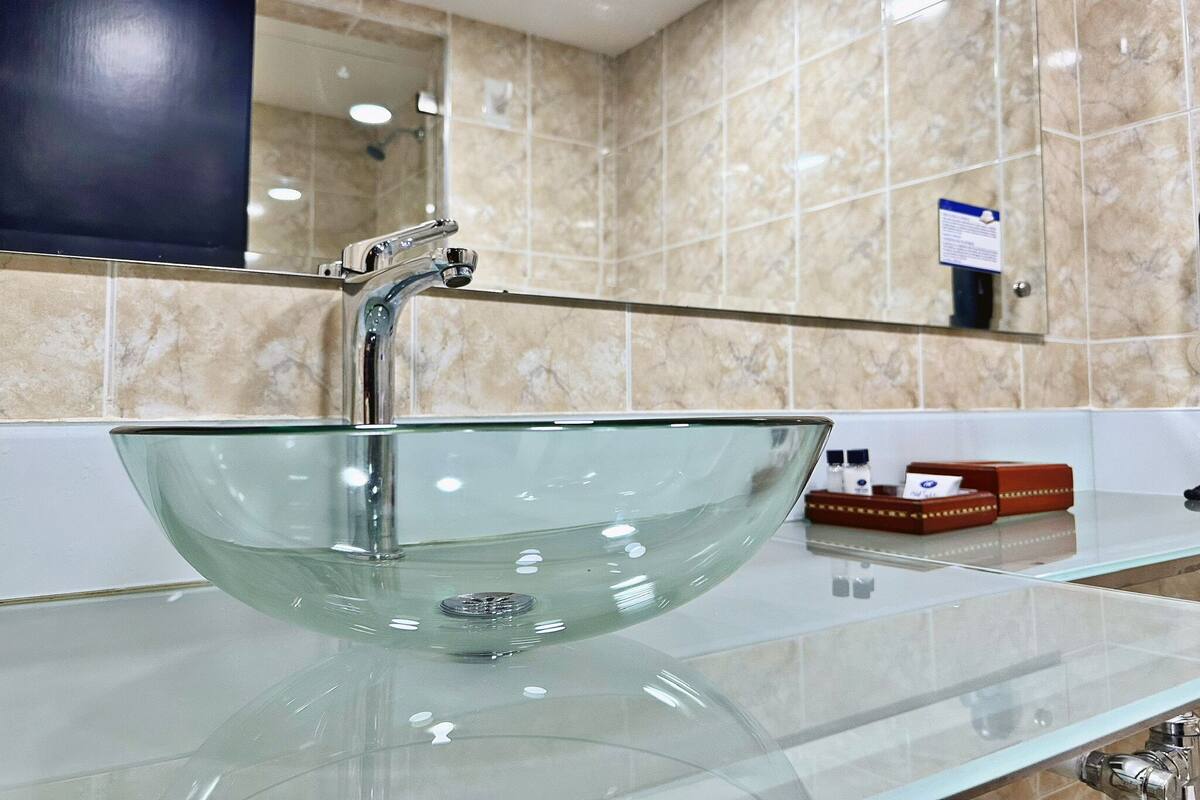 Een moderne badkamer met een glazen wasbak, een chromen kraan en een grote spiegel boven de wasbak.