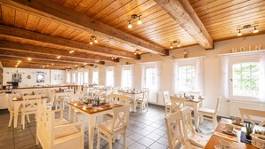 Un comedor espacioso con vigas de madera, sillas blancas y mesas dispuestas para comer.