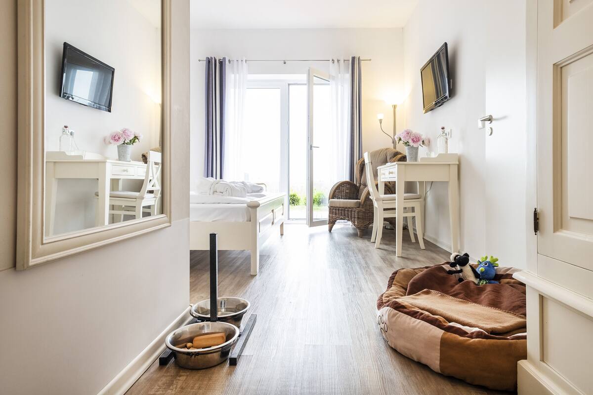 Ein Hotelzimmer mit Bett, Schreibtisch, Sessel, Fernseher und Badezimmer mit Spiegel und Waschbecken.