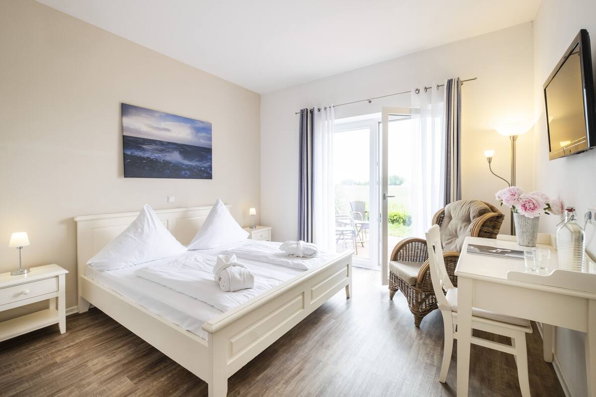 Ein Hotelzimmer mit Bett, Schreibtisch, Stuhl, einem Fenster mit Vorhängen und einem Gemälde an der Wand.