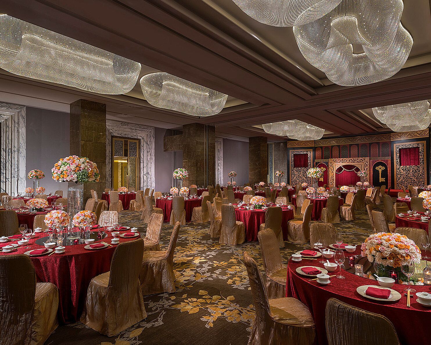 A banquet hall with round tables covered in red tablecloths, arranged in rows.
