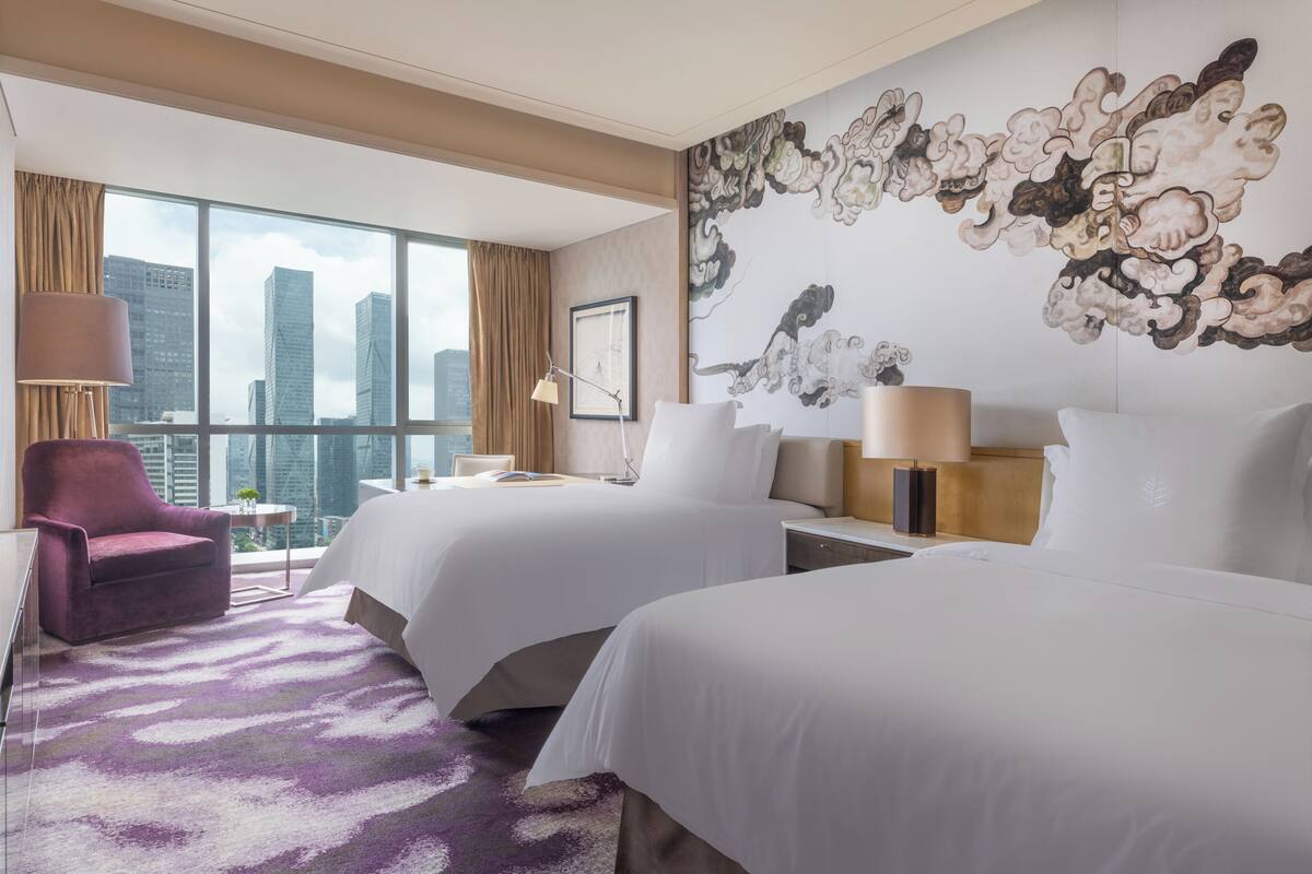 A hotel room with two beds, a large window with a city view, a purple armchair, and a decorative wall piece.