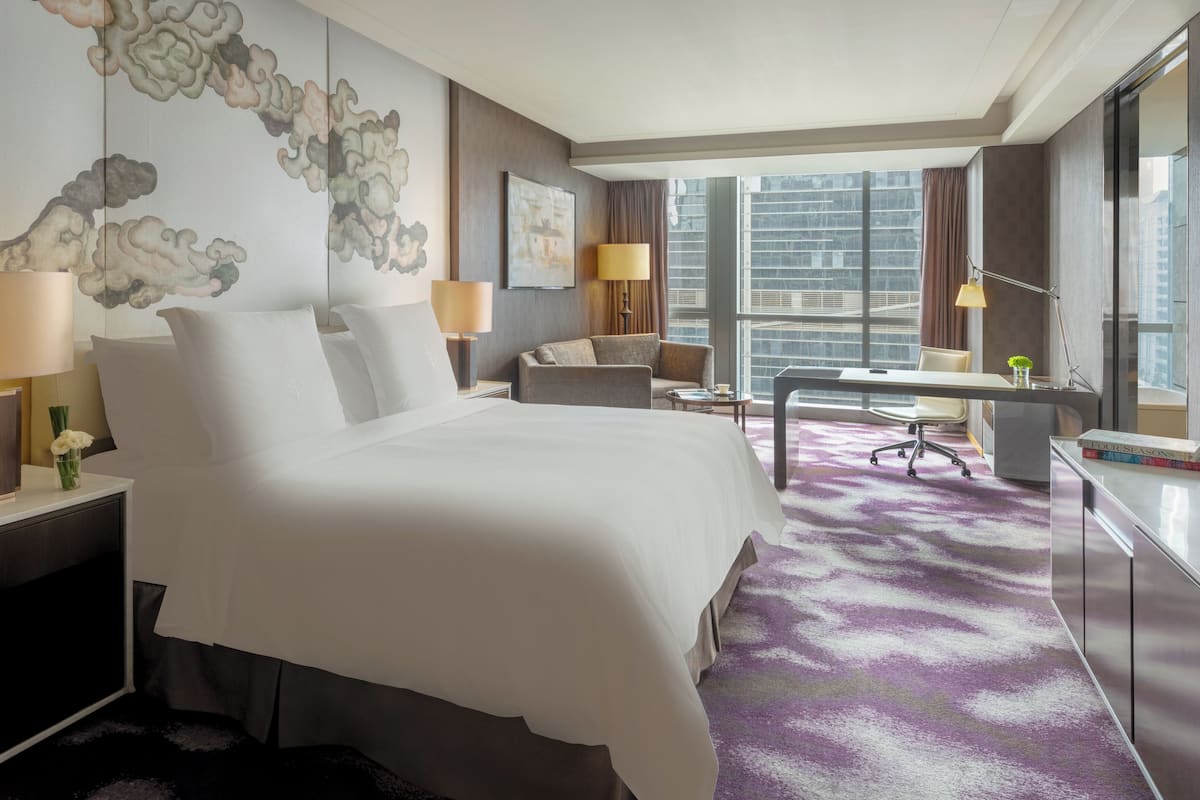 A hotel room with a large bed, a desk, a chair, and a view of the city.