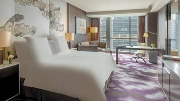 A hotel room with a large bed, a desk, a chair, and a view of the city.