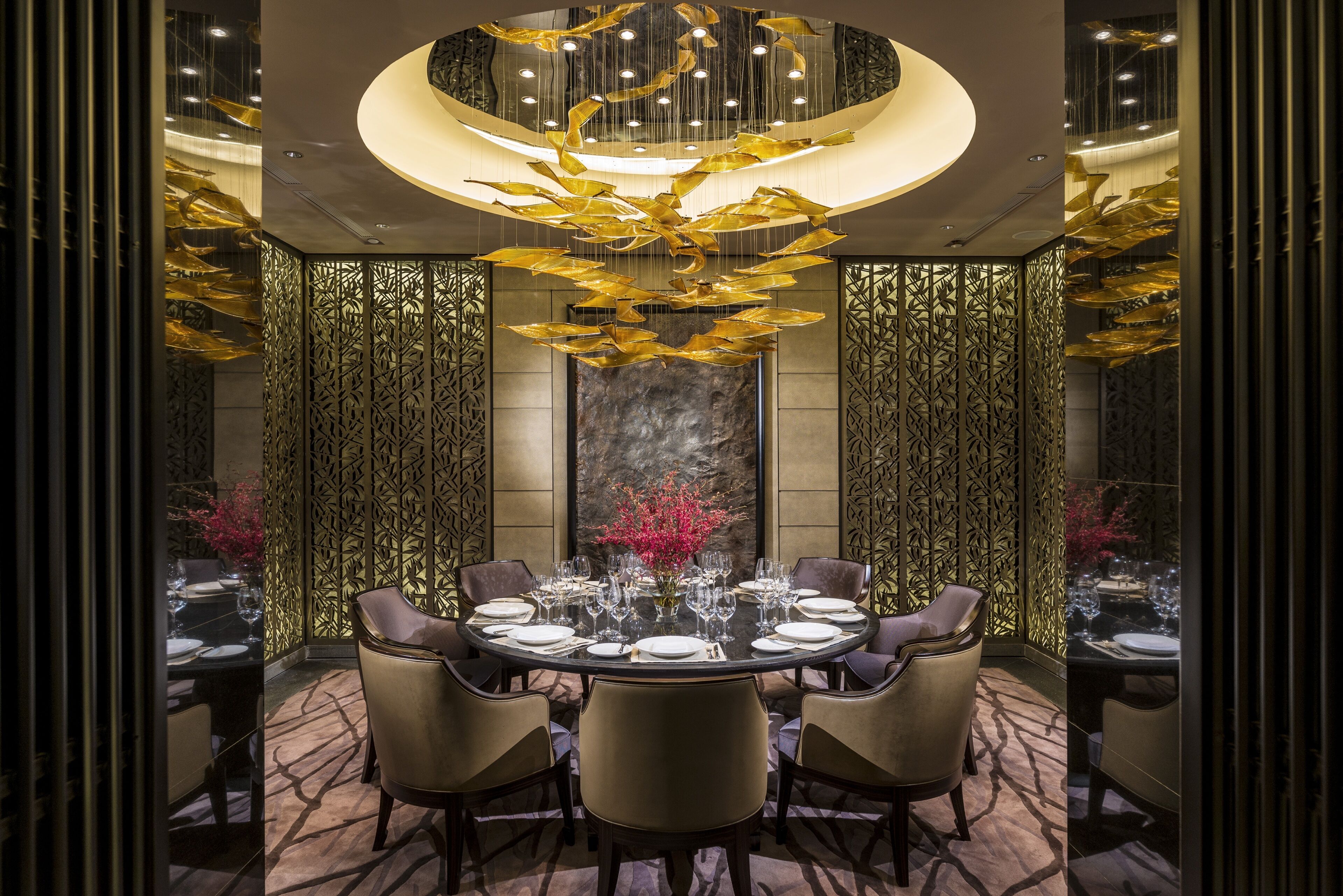 A dining area with a round table set for six, surrounded by chairs, with a decorative chandelier above.