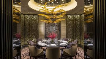 A dining area with a round table set for six, surrounded by chairs, with a decorative chandelier above.