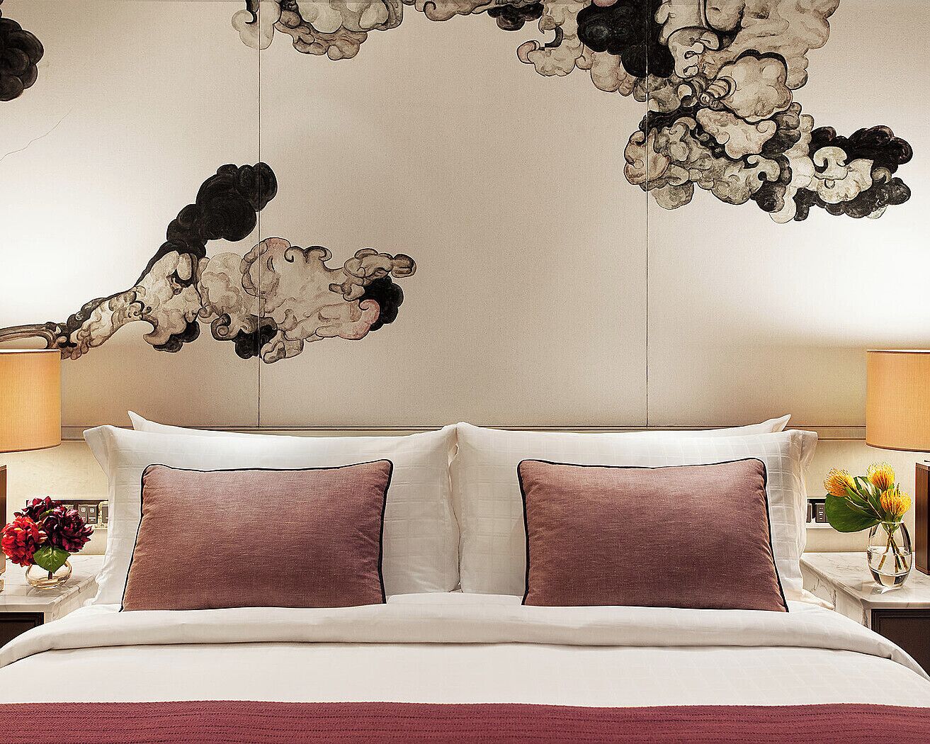 A hotel room with a large bed, two pillows, a nightstand with a lamp, and a wall decoration.