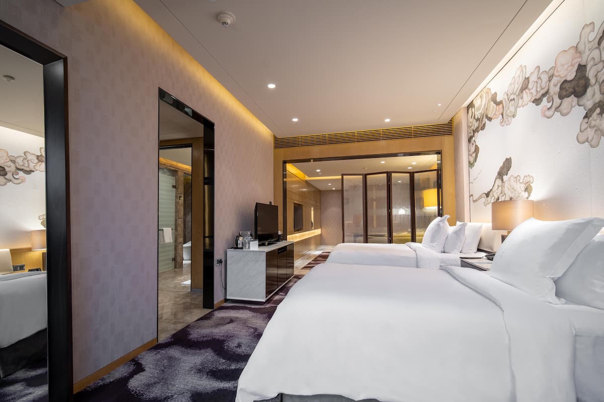 A hotel room with two beds, a desk, a TV, and a bathroom visible through an open door.