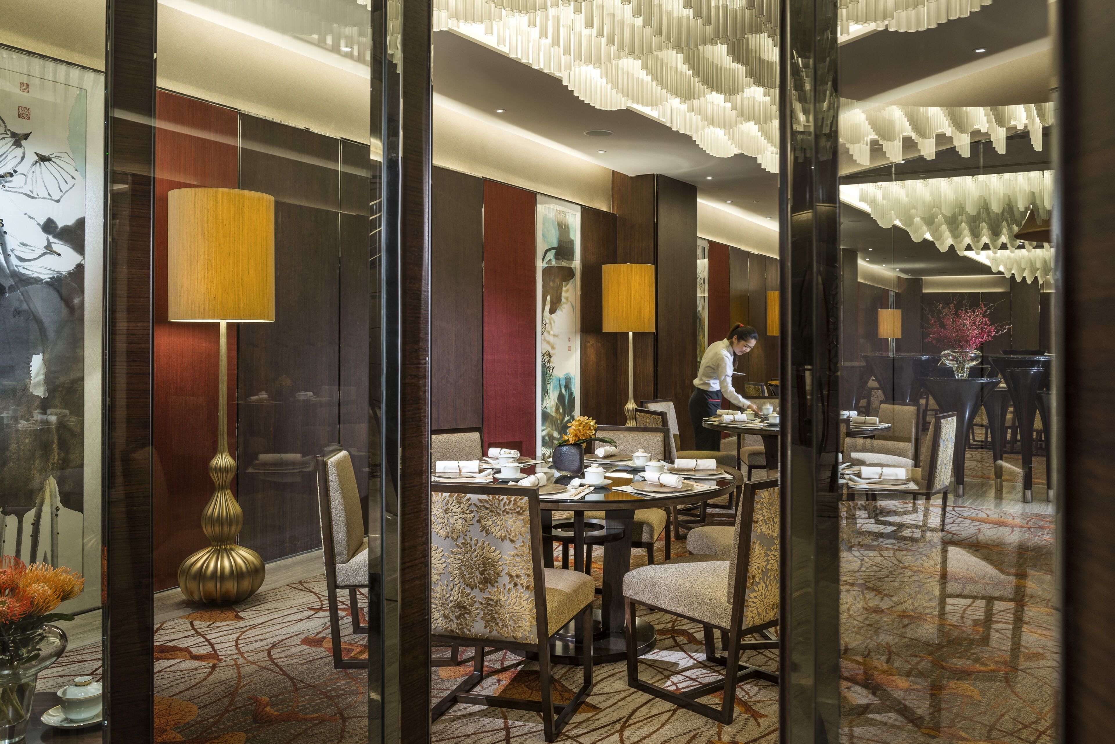 A hotel dining area with round tables, chairs, and a waiter.
