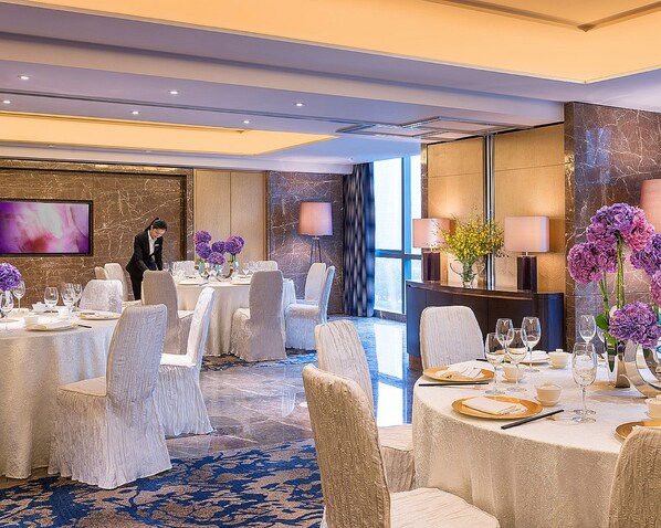 Un comedor de hotel con mesas redondas, sillas y un miembro del personal de servicio.