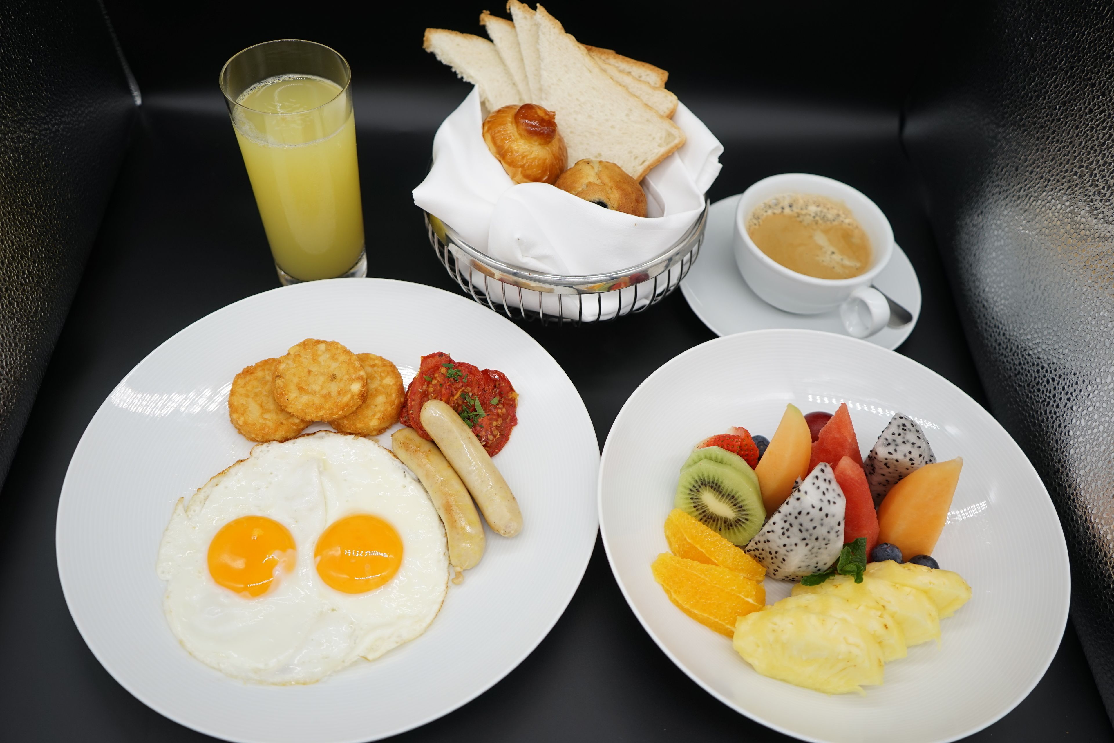 A breakfast tray with eggs, sausages, toast, fruit, and a cup of coffee.