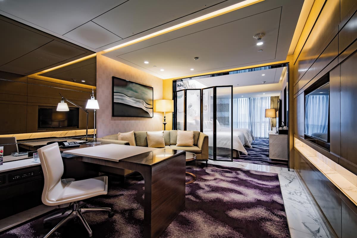 A modern hotel room with a desk, sofa, and a large window.