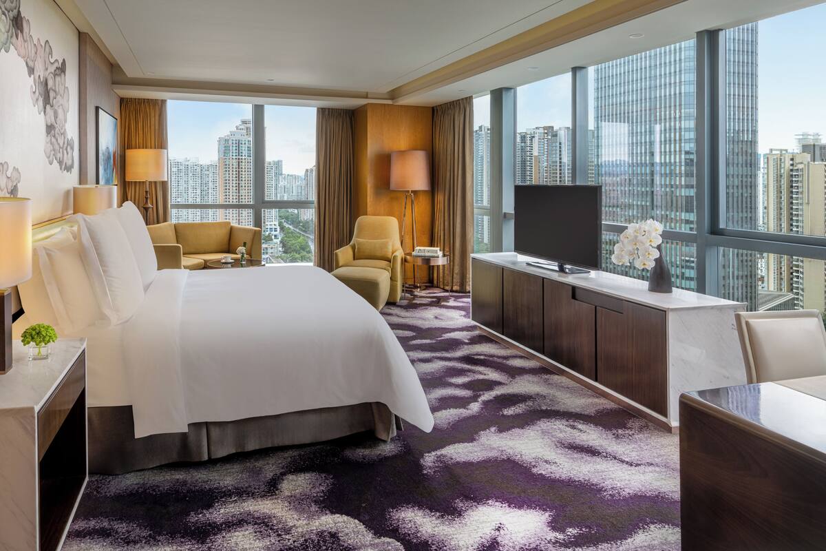 A hotel room with a large bed, a desk, a TV, and a view of the cityscape.