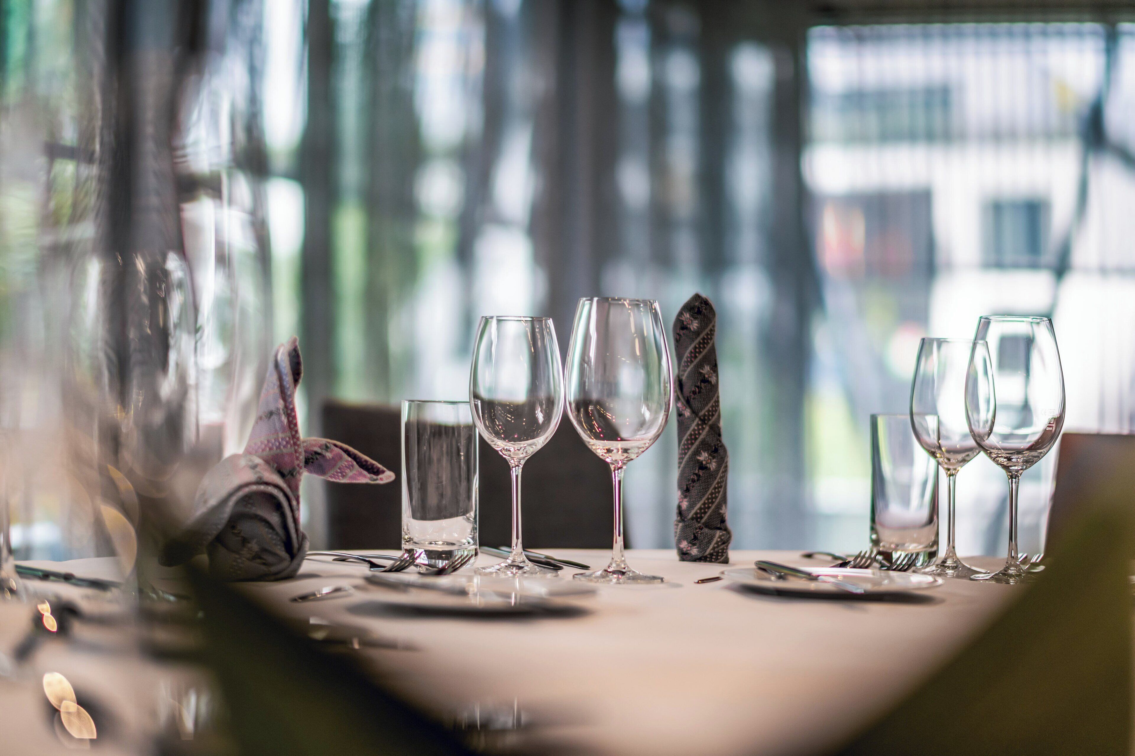 A table set for dining with clear glassware and cutlery, a patterned napkin, and a view of the outdoors through a window.