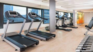 A modern gym with treadmills, weights, and a city view.