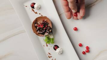 A dessert on a white plate with a hand placing red berries.