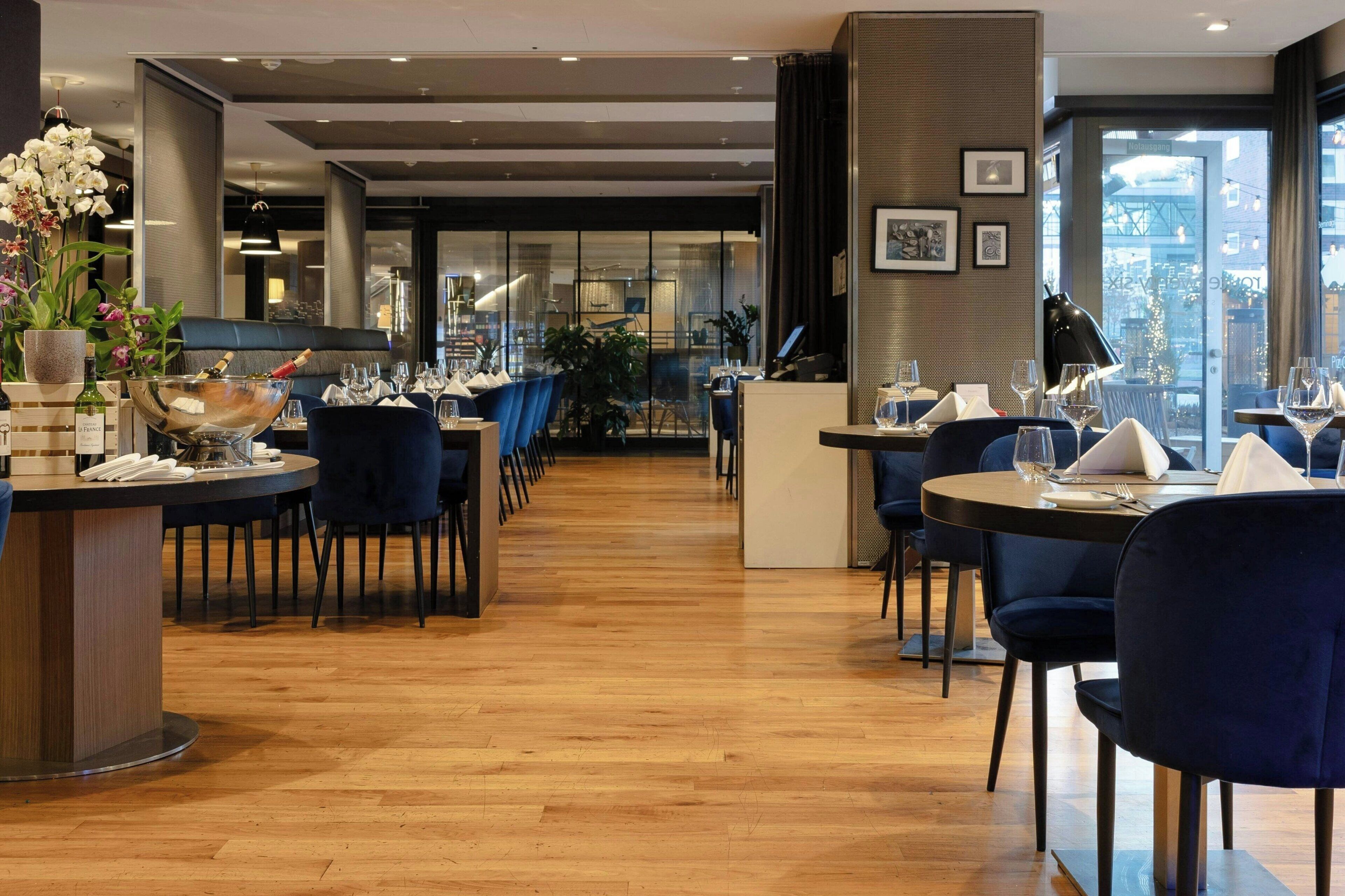 A modern restaurant with wooden flooring, blue upholstered chairs, and a central bar area.