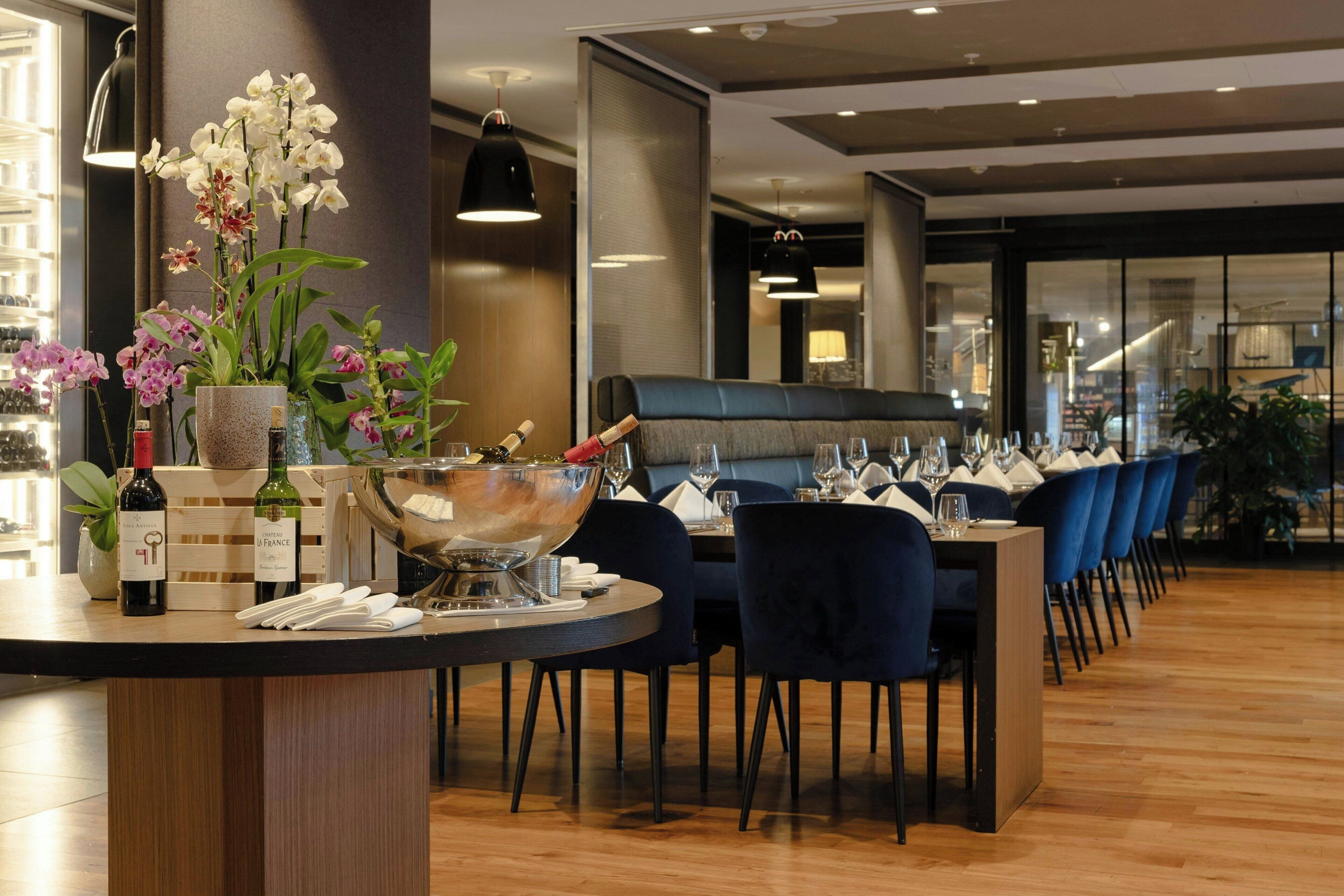 A modern restaurant with a long counter, blue chairs, and a variety of flowers.