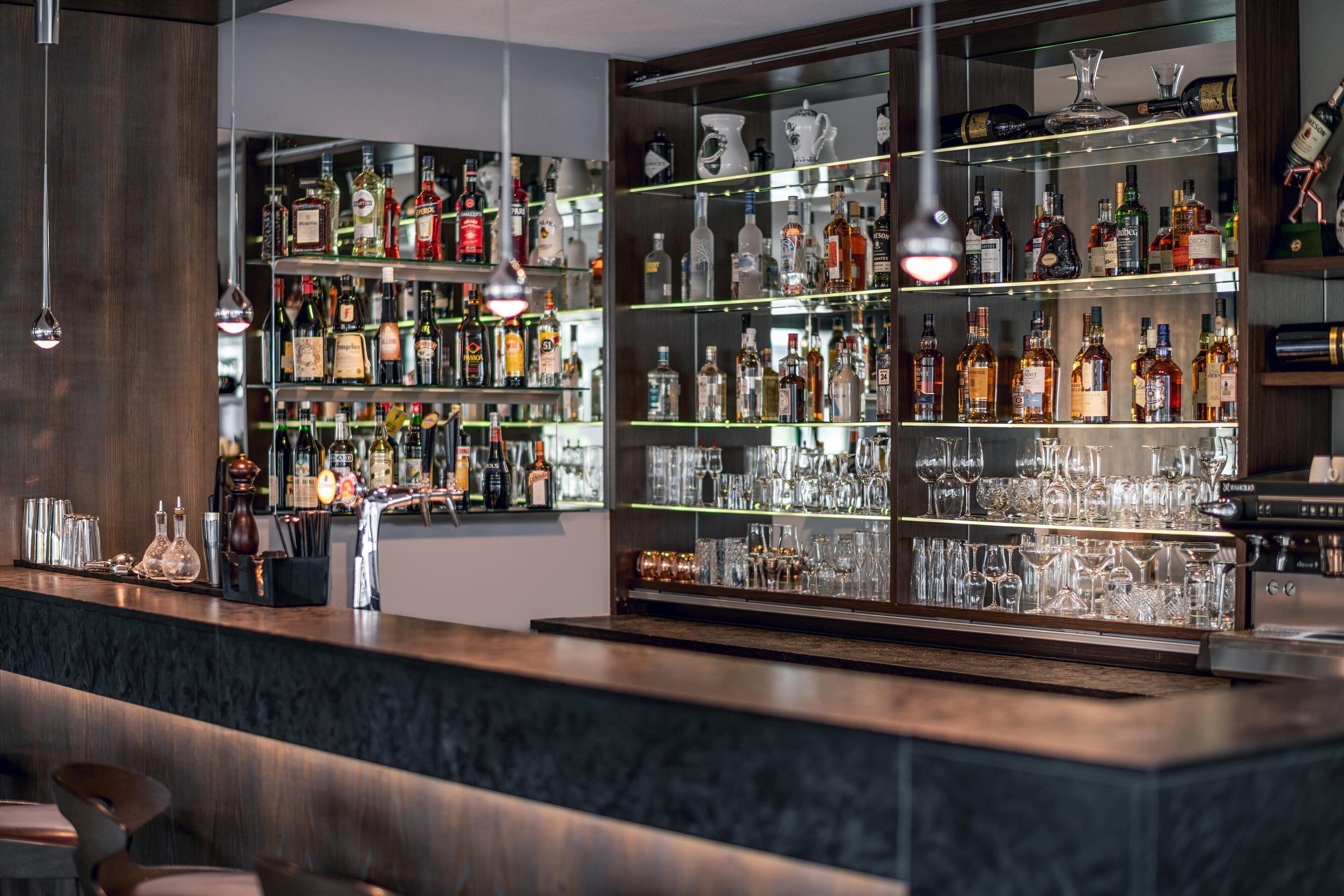 A bar area with shelves of liquor bottles and glasses, a marble countertop, and hanging pendant lights.