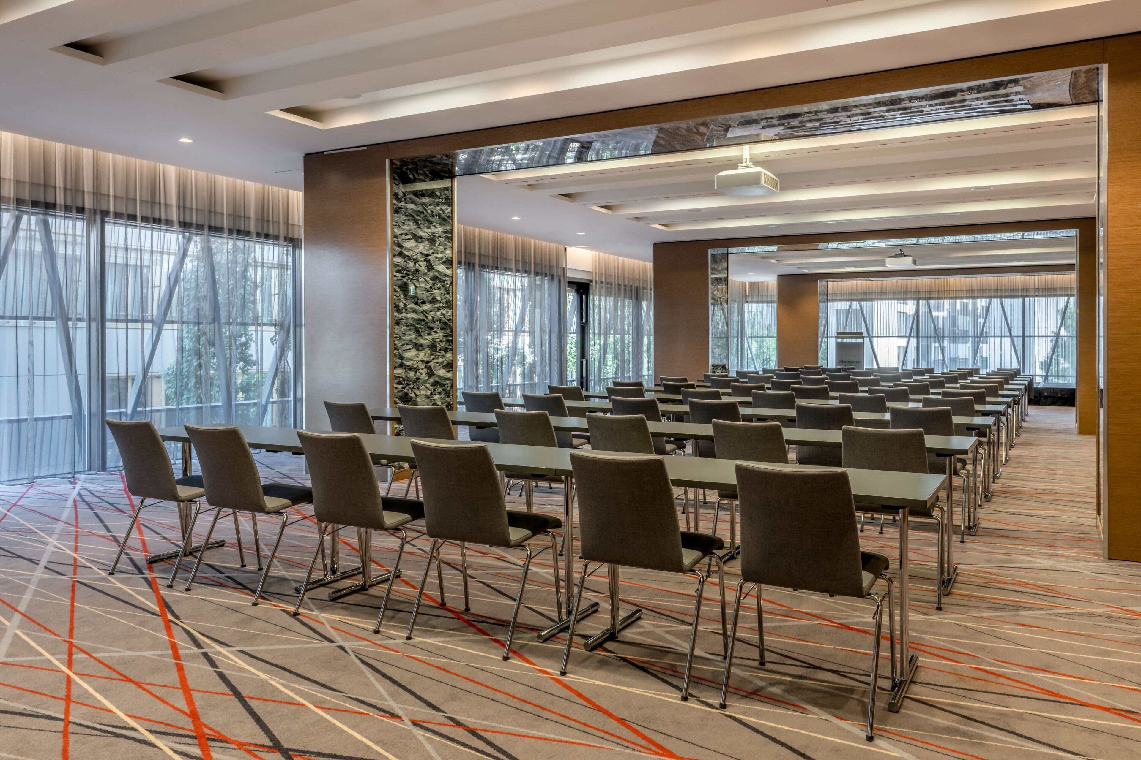 A conference room with rows of tables and chairs, large windows, and a patterned carpet.