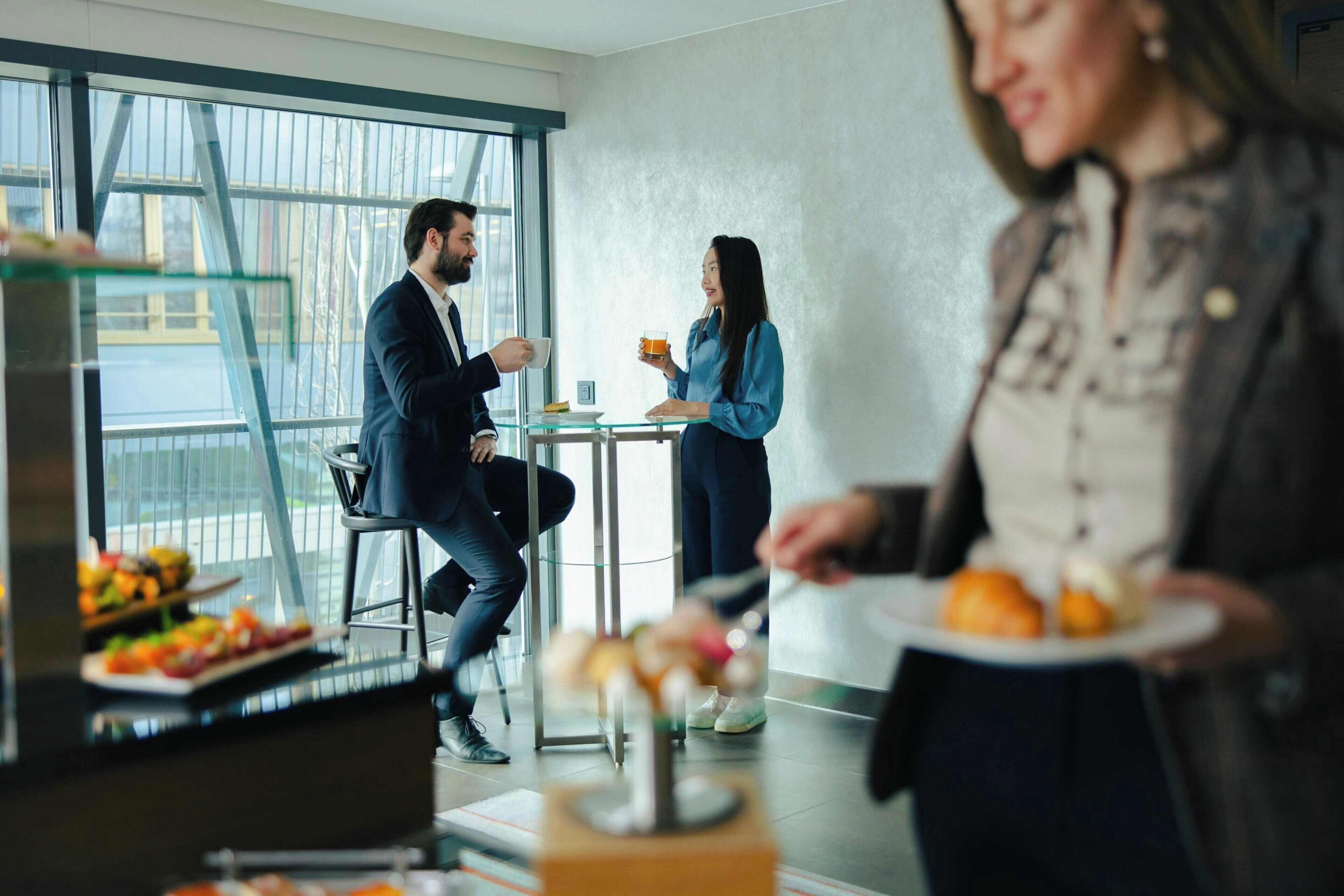 A modern interior with a glass partition, a dining table, and a person holding a plate.