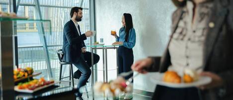 A modern interior with a glass partition, a dining table, and a person holding a plate.