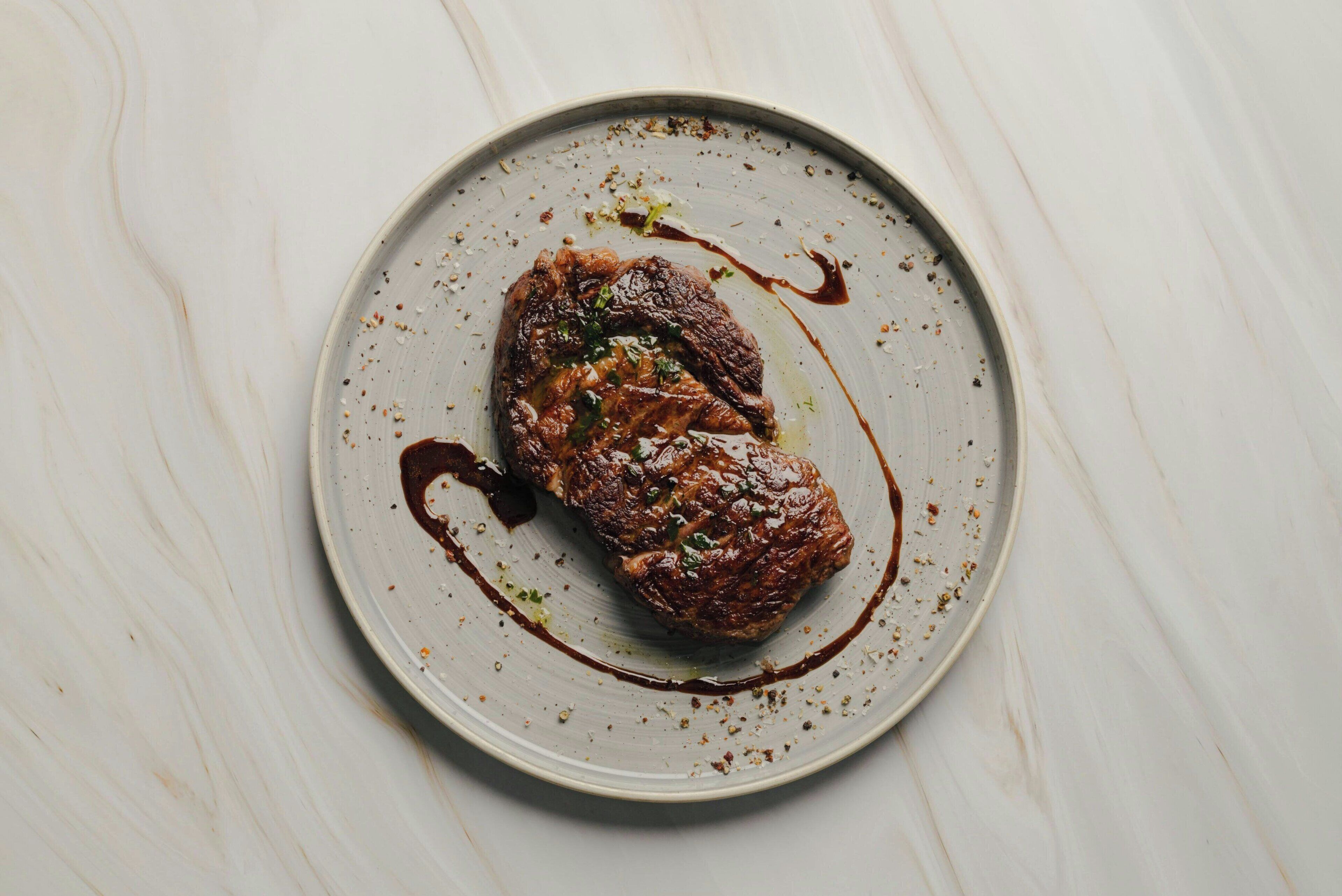 Un plato con un trozo de carne y salsa sobre una superficie de mármol blanco.