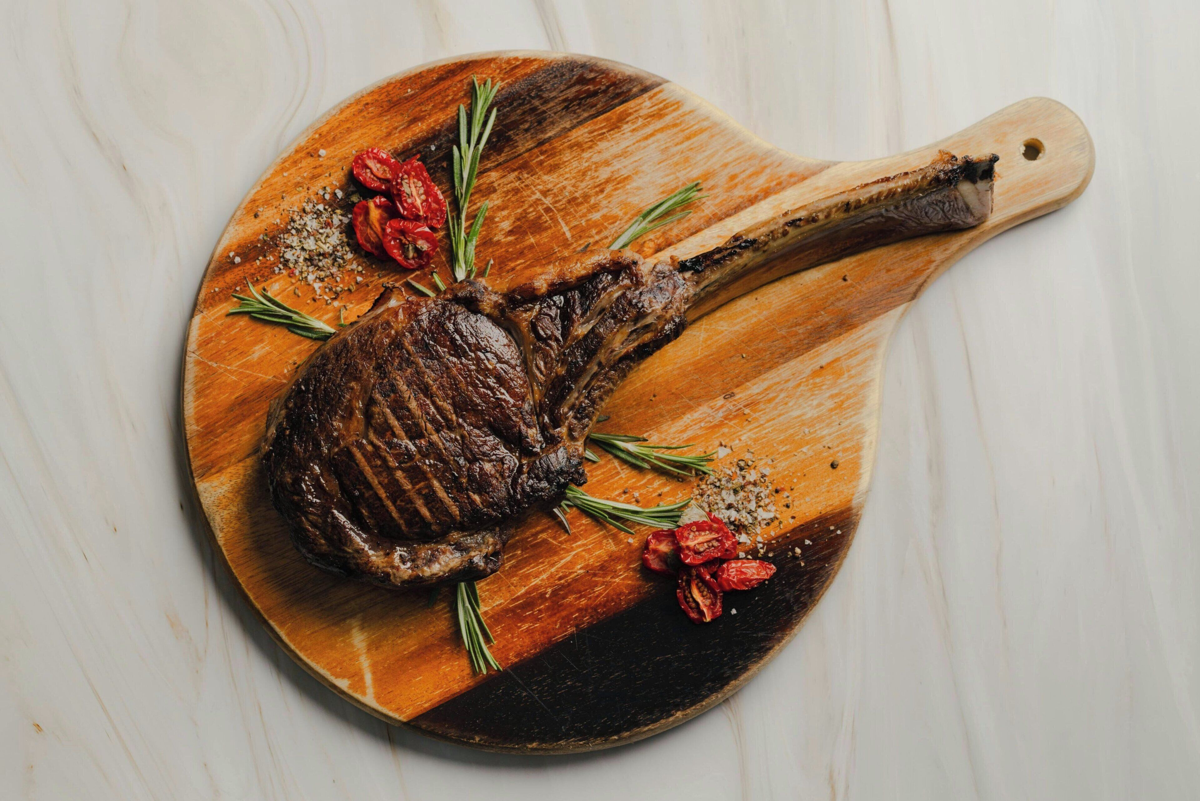 Un bistec sobre una tabla de madera con romero y tomates cherry.