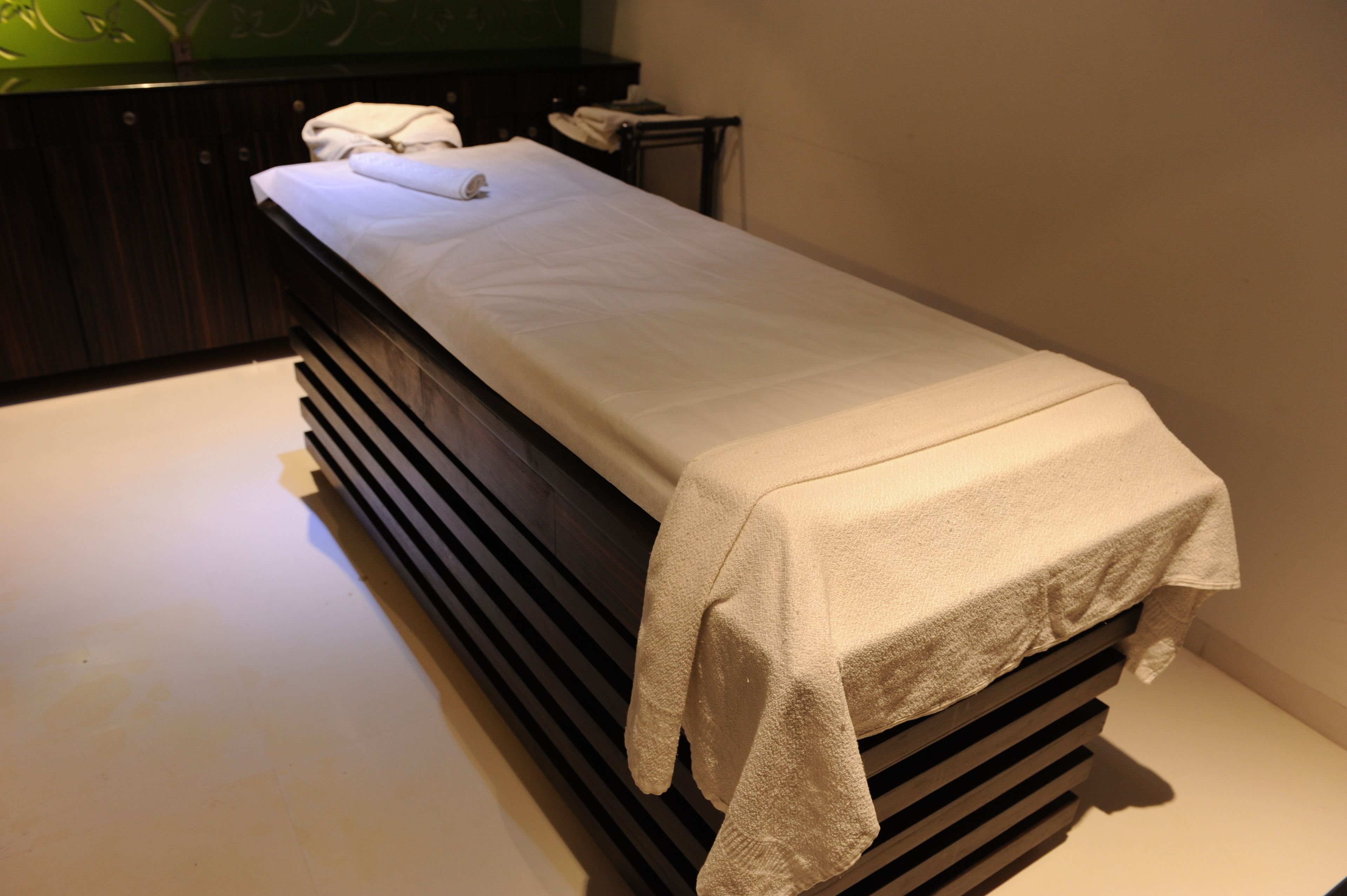 Een enkel bed met een wit laken in een kamer met een donker houten hoofdeinde en een groene wand.