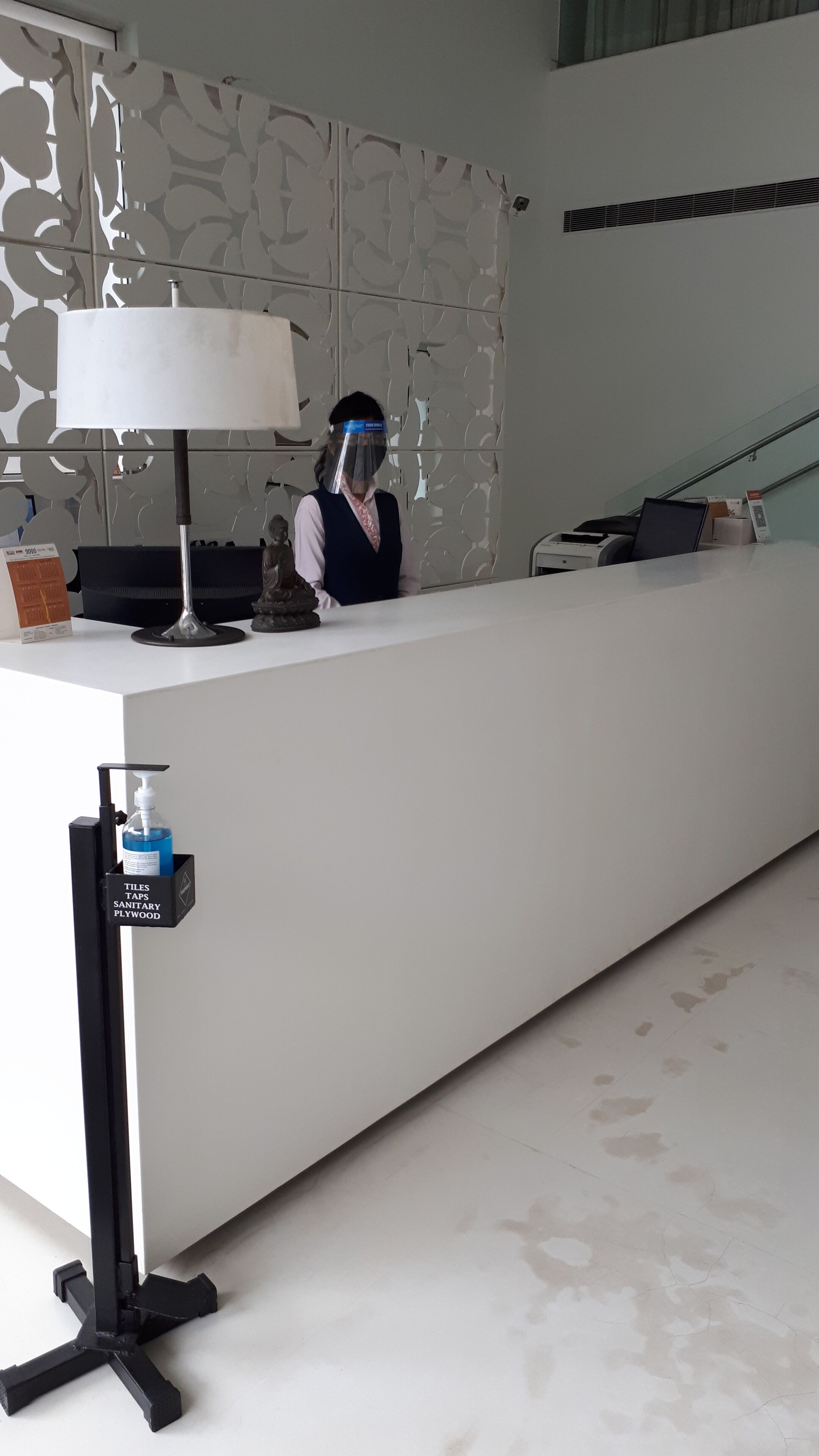 A reception desk with a white counter, a lamp, a statue, and a hand sanitizer dispenser.