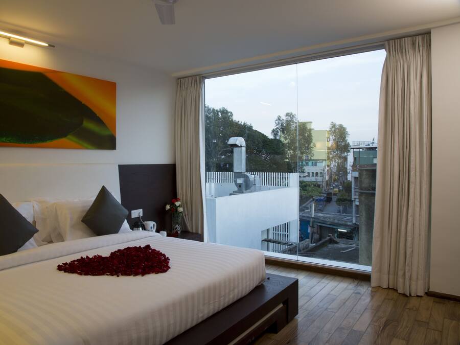A modern hotel room with a large bed, a view of the city through a large window, and a painting on the wall.
